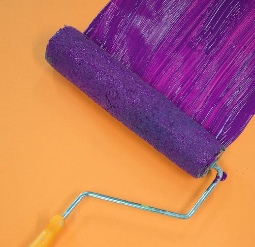 Image of a paint roller applying a purple color onto an orange interior house wall